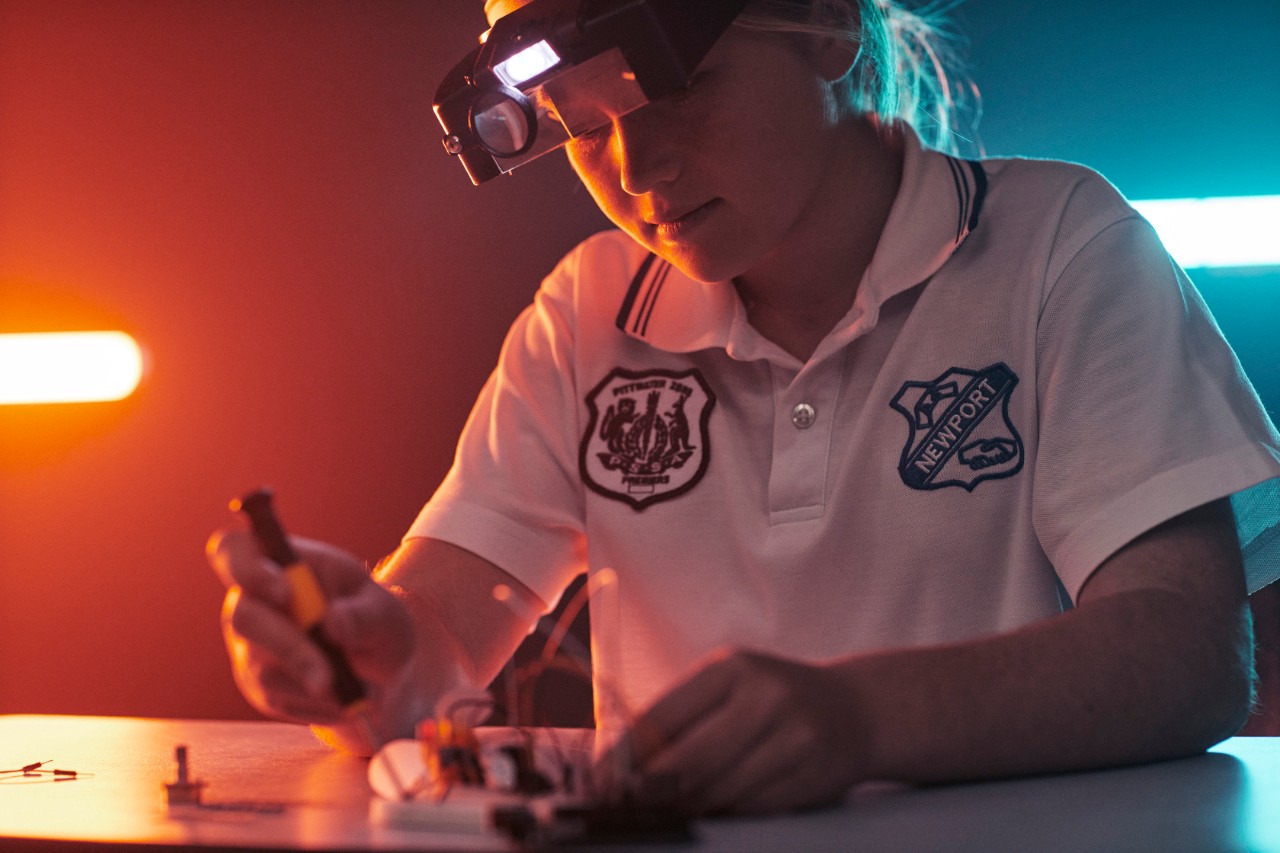 200716_DoE_Maths__SH08_001_RGB_150dpi1 Female student wearing glasses with a headlamp, working with a screwdriver at a desk.